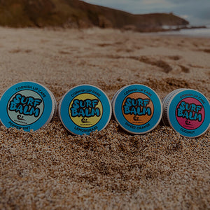 Four tins of Surf Balm on a sandy beach