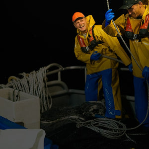 Two men on a fishing boat at night, wearing life jackets and various waterproof garments